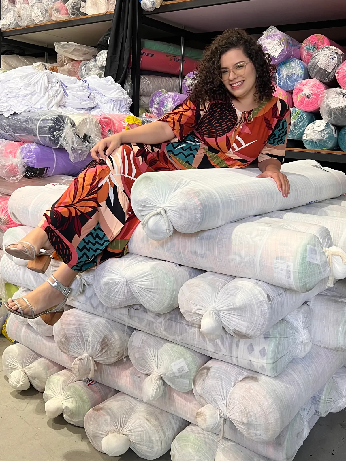 Mulher sorrindo sentada sobre rolos de tecido